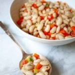 A white bowl and silver spoon filled with tuscan beans, red pepper, and celery.