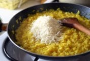 Skillet on the stove filled with risotto alla Milanese, a pile of cheese, and a wooden spoon