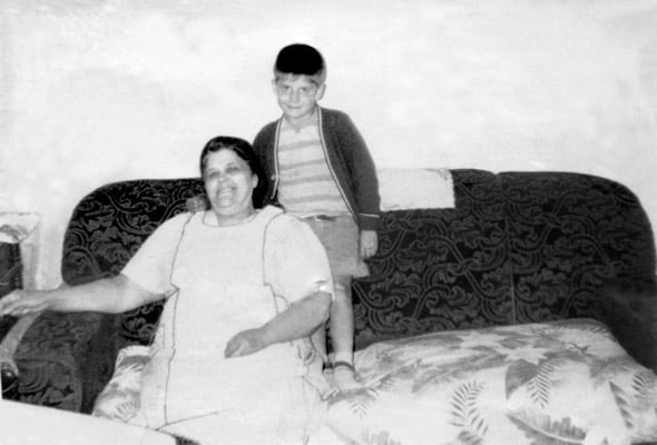 An old woman in a dress and apron with a small boy standing beside her.