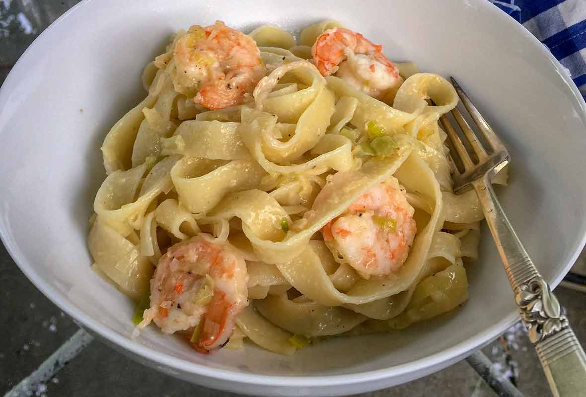 A bowl filled with shrimp and leek Pasta--large shrimp, wide noodles, chopped leeks, and cheese