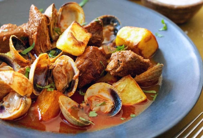 A blue bowl filled with Portuguese pork with clams and fried potato cubes.