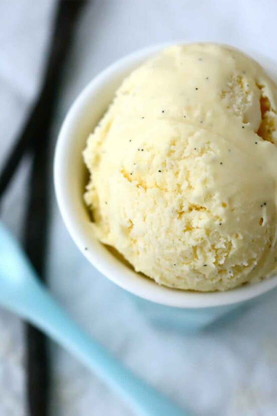 A white bowl filled with French vanilla ice cream with a blue spoon resting beside.