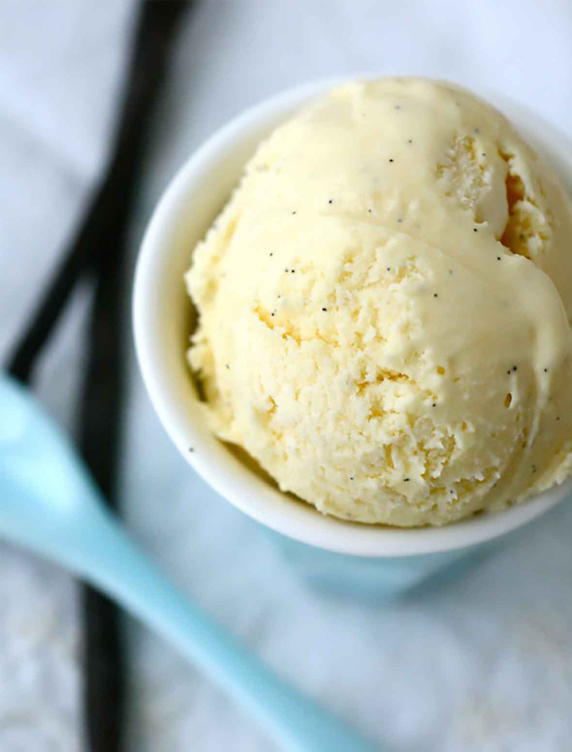 A white bowl filled with French vanilla ice cream with a blue spoon resting beside.