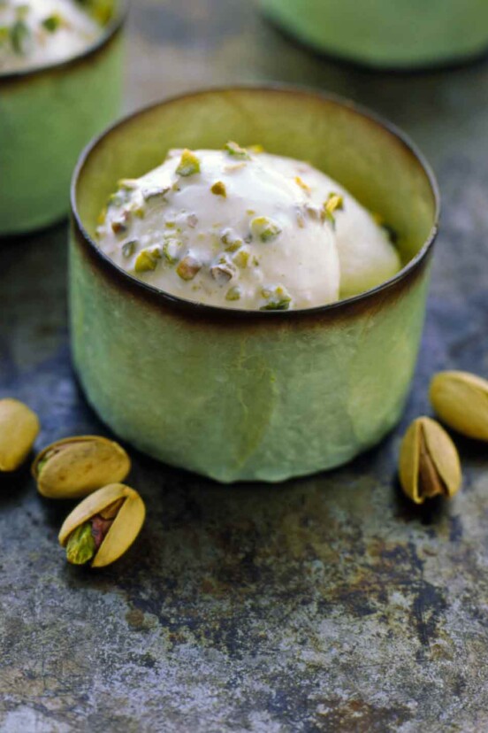 A few green cups filled with pistachio gelato with five pistachios beside.