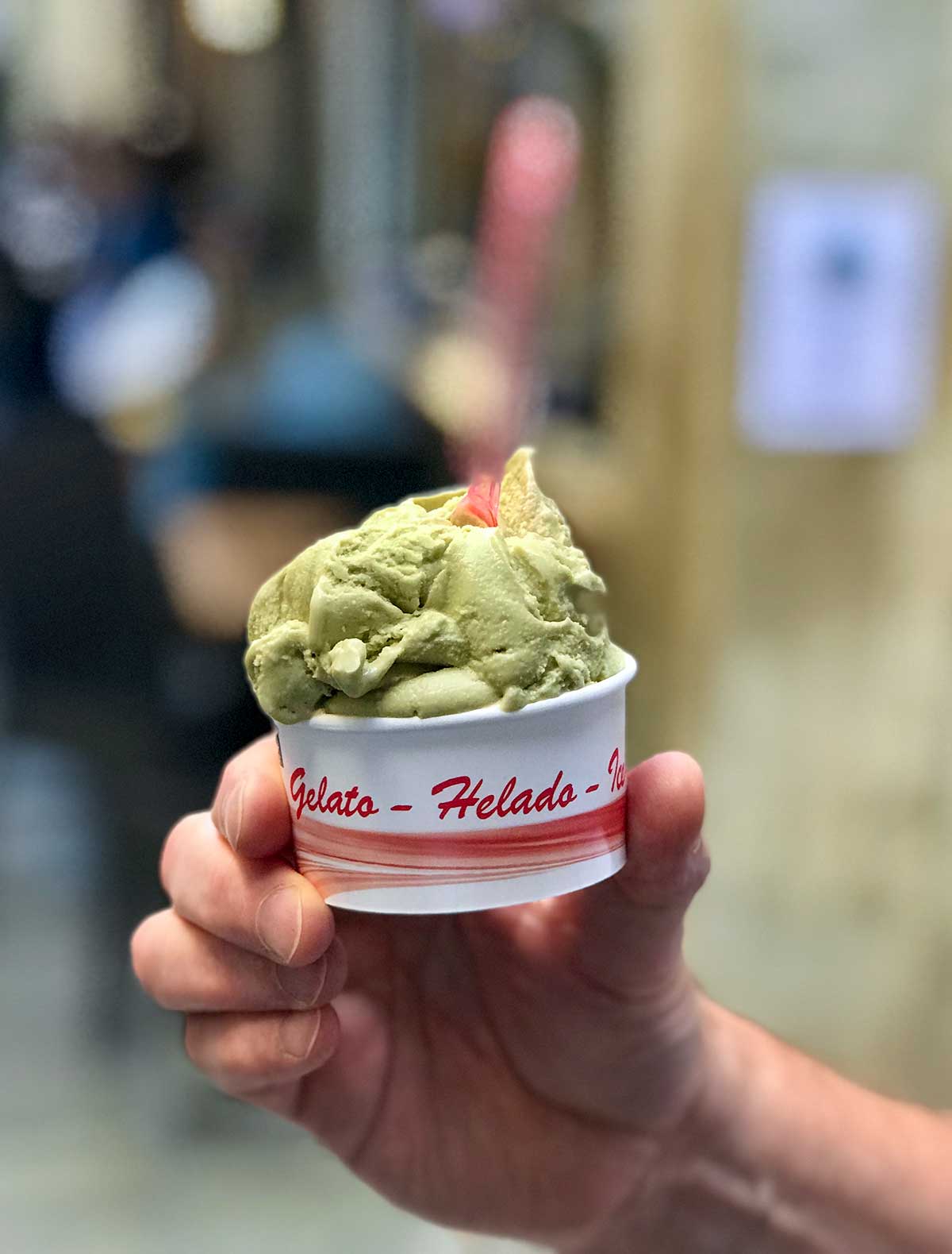 A man's hand holding a cup of pistachio gelato in Venice, Italy