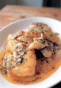 Plate of fried salt cod in a garlic-pepper sauce, on top are pepper flakes and sliced garlic cloves