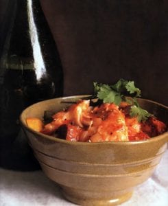 A brown ceramic bowl filled with Portuguese fish chowder, made with fish, potatoes, chouriço, tomatoes, and cilantro.