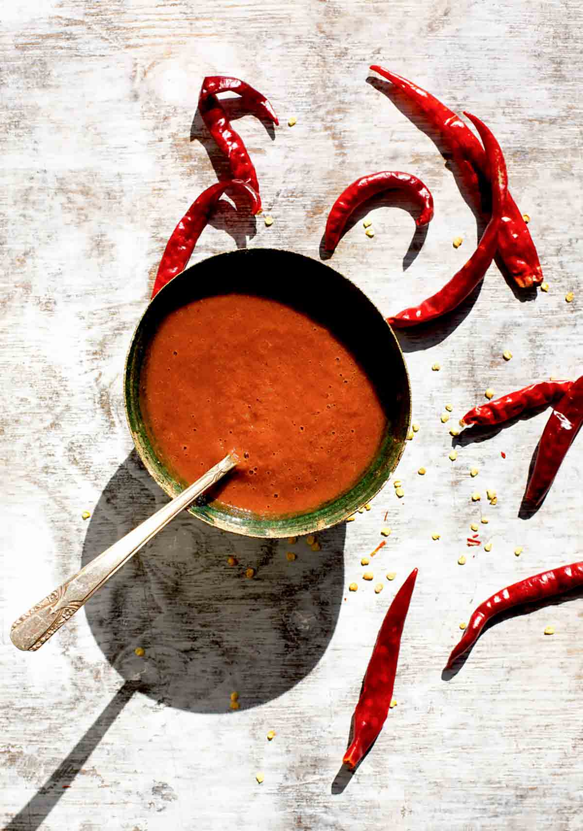 A green bowl filled with Portuguese piri-piri hot sauce, a few dried red chiles on the side