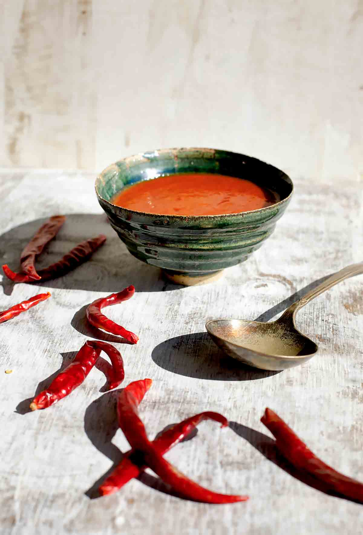 A green bowl filled with Portuguese piri-piri hot sauce, a few dried red chiles on the side