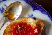 A slice of toast schmeared with Portuguese tomato jam on a decorative plate with a spoon resting beside it.