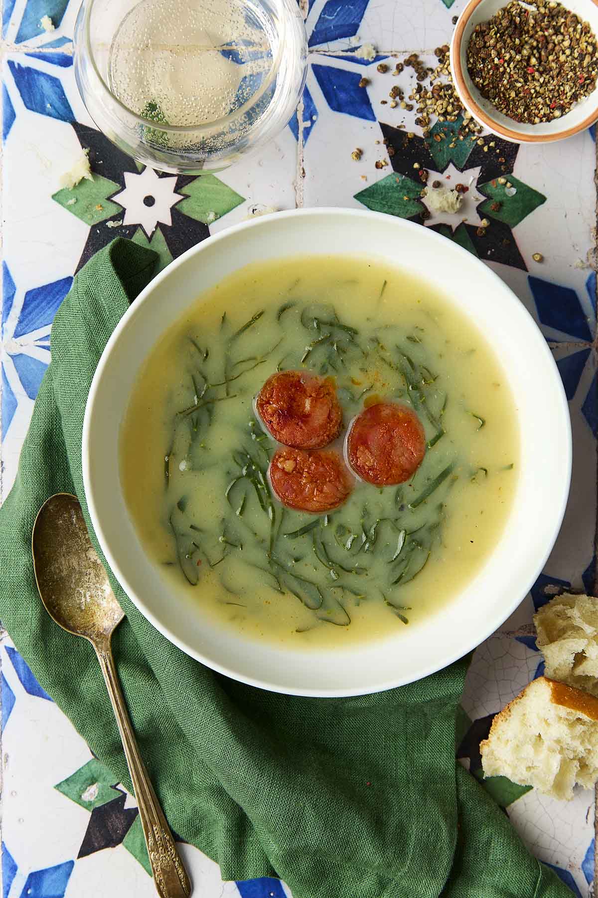 A white bowl of caldo verde, or Portuguese kale soup (green broth) with thinly sliced kale and three chourico coins floating in the center.