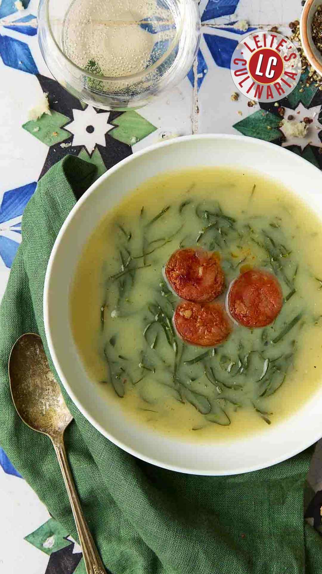 A white bowl of caldo verde, or Portuguese kale soup (green broth) with thinly sliced kale and three chourico coins floating in the center.