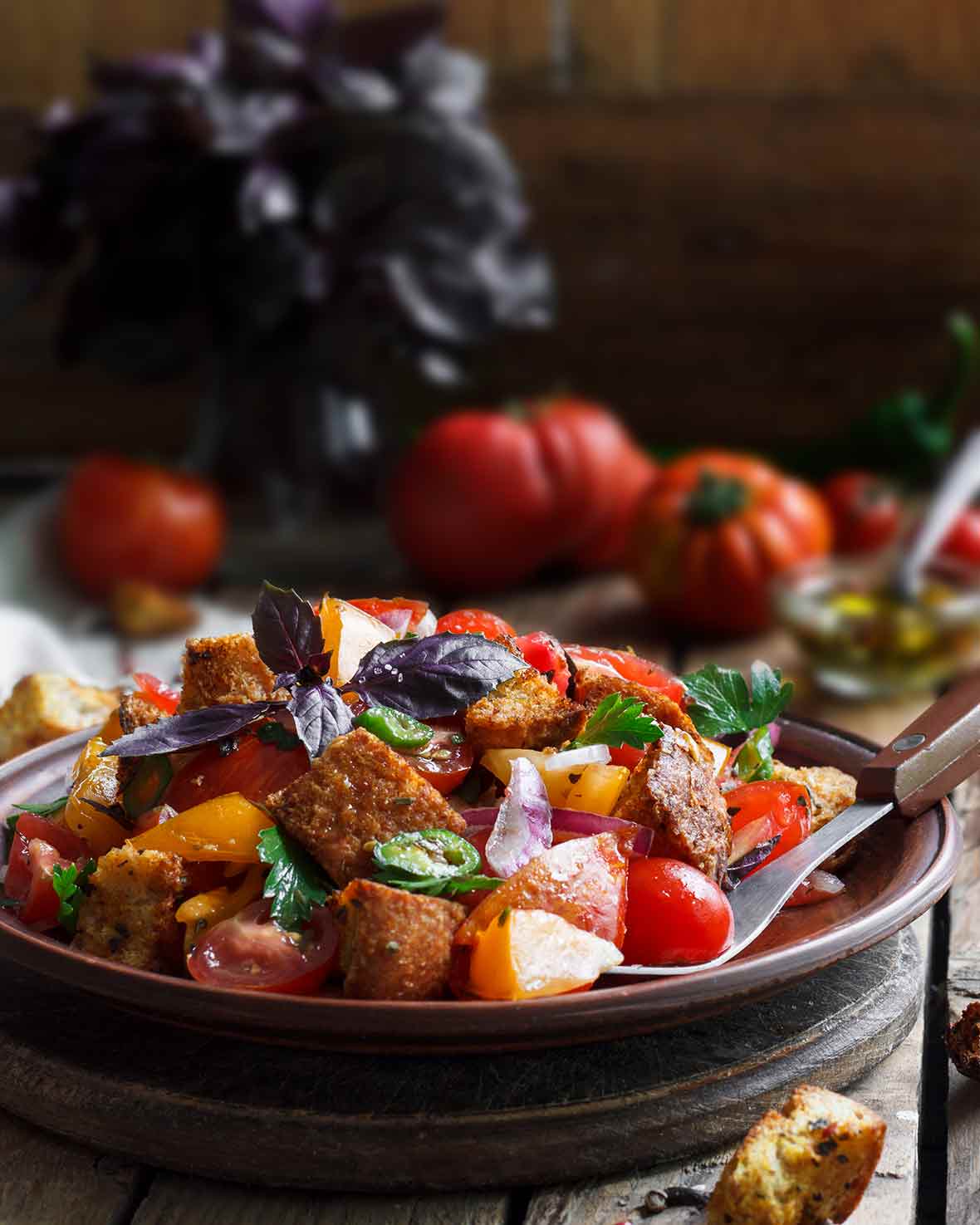 Wood bowl of panzanella from Ina Garten with bread chunks, tomatoes, peppers, cucumbers, basil, and parsley