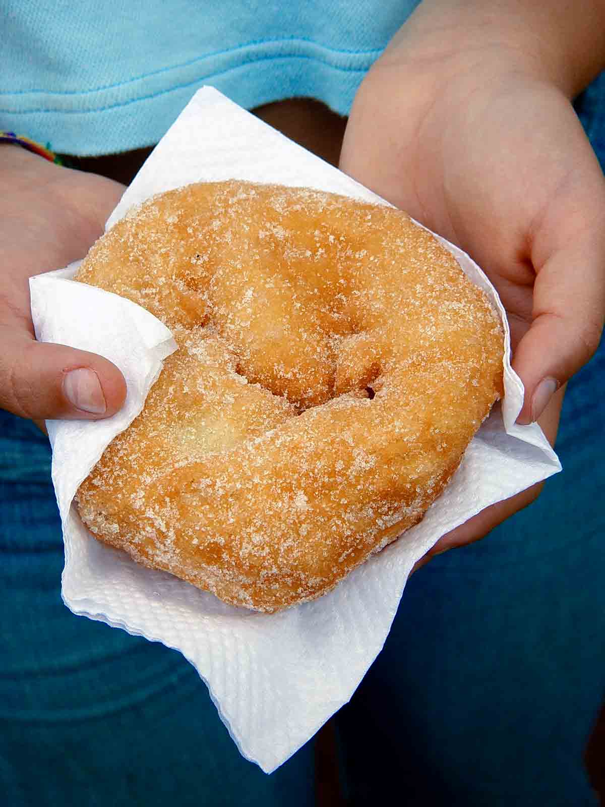 A child holding a malassadas, or Portuguese doughnut, in a paper napkin.