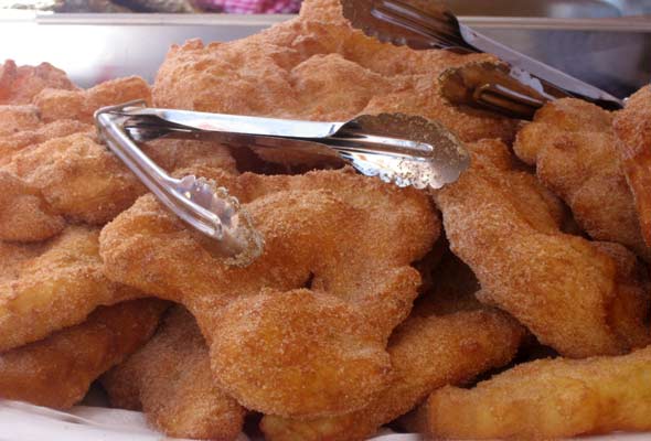 A pile of malassadas or Portuguese doughnuts with a pair of metal tongs