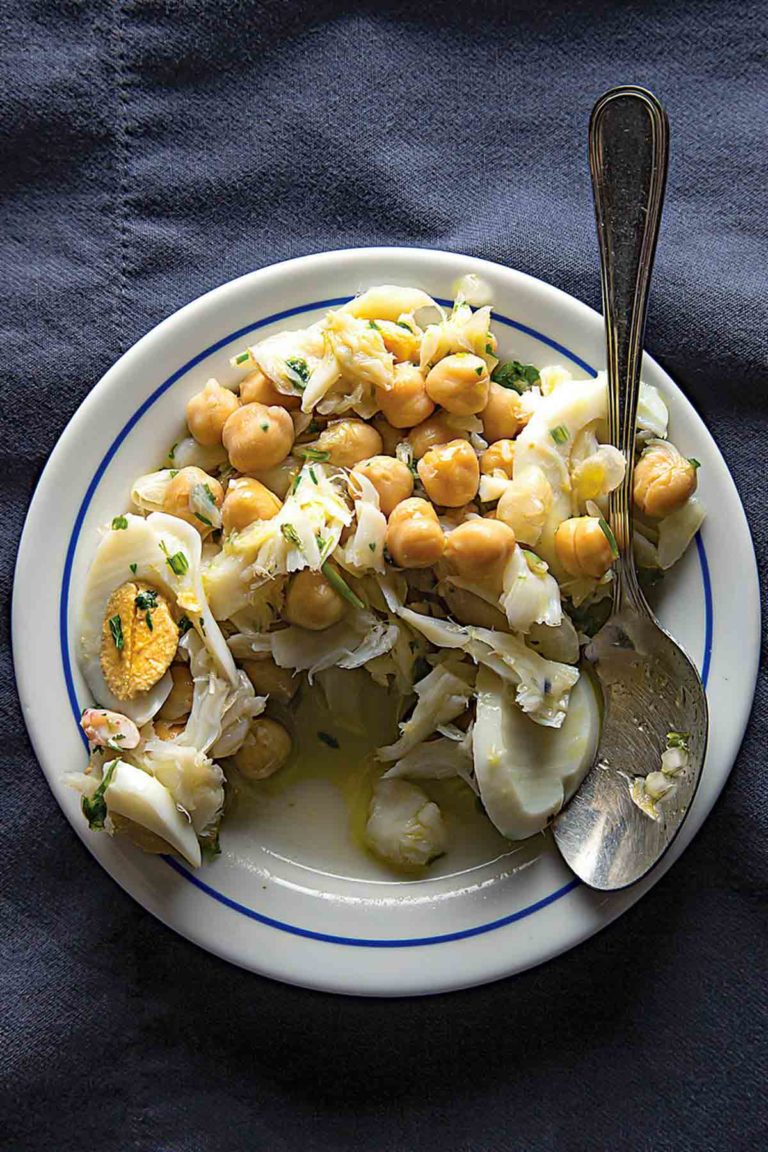 Portuguese Salt Cod and Chickpea Salad on a white plate with a silver serving spoon resting on the edge of theplate.