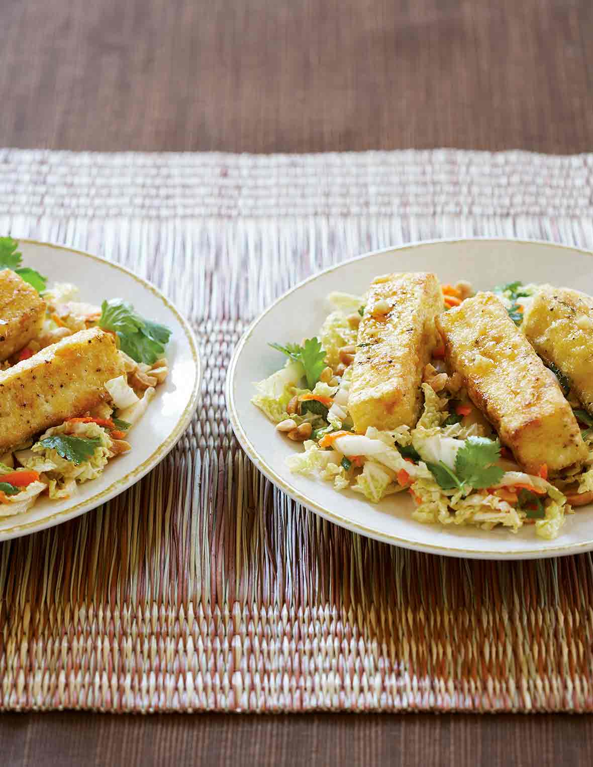 Two plates of warm cabbage salad with fried crispy tofu, carrots, cilantro on woven placemats