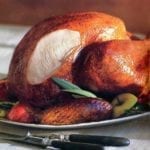 A classic roast turkey on a platter with pieces of apple and rosemary sprigs tucked around it.