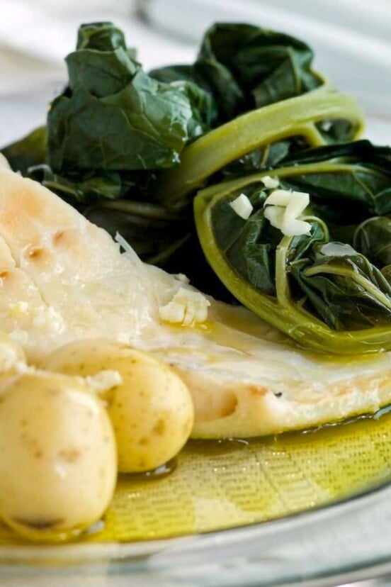A white plate of bacalhau consoada or Portuguese Christmas Eve cod, with salt cod, small potatoes, and blanched kale.