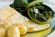 A white plate of bacalhau consoada or Portuguese Christmas Eve cod, with salt cod, small potatoes, and blanched kale