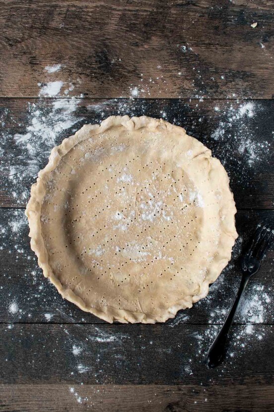 An unbaked lard and butter pie crust, with fork pricks all over on a wooden table.
