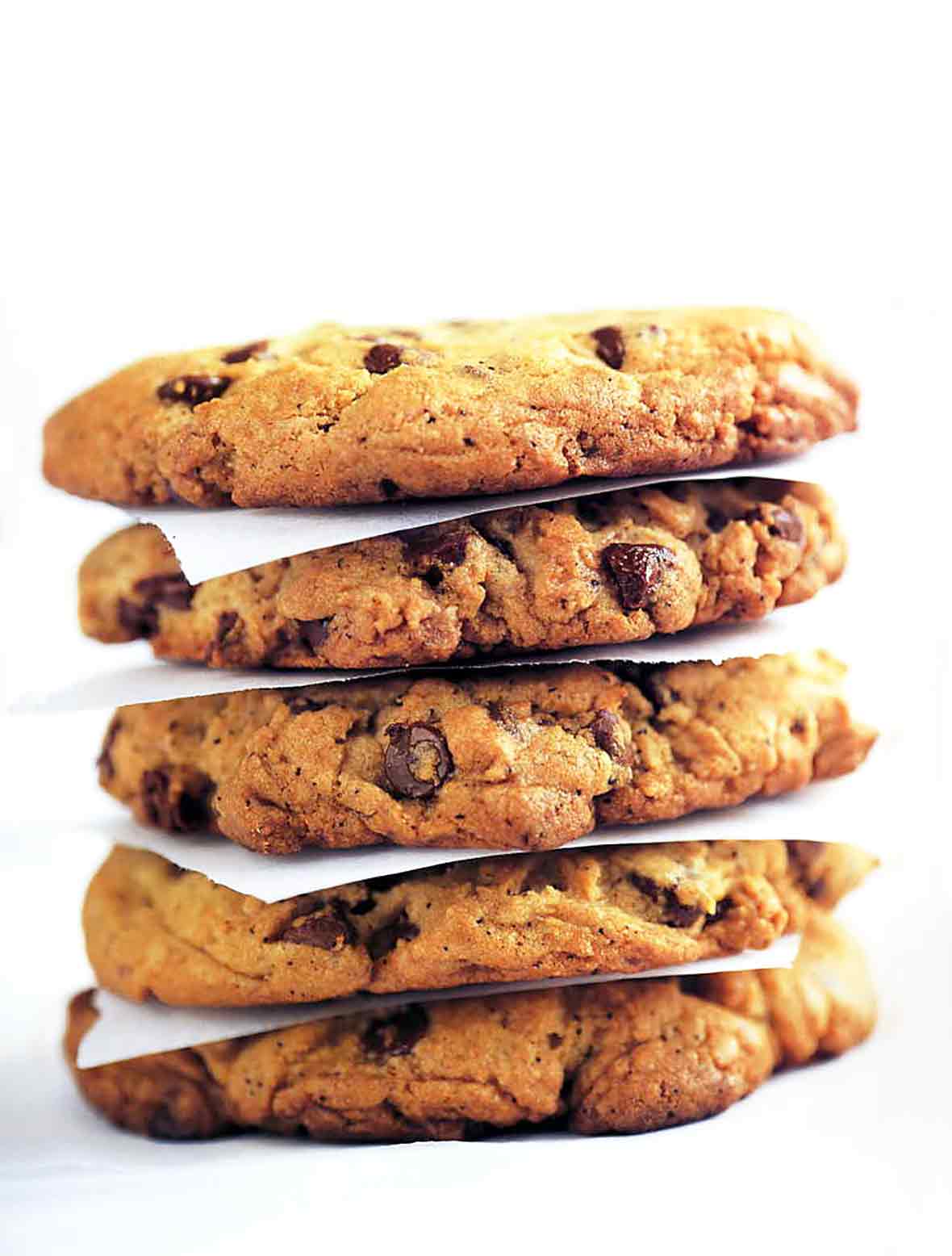 A stack of Neiman Marcus chocolate chip cookies separated by pieces of parchment.
