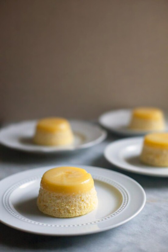Four white plates, each topped with a lemon steamed pudding.