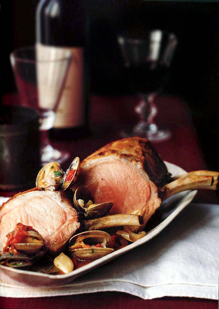 Portuguese-Style Pork Roast with Clams on a white platter with a wine glass and open bottle of red wine in the background.