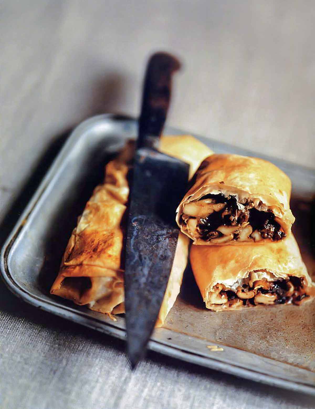 Two mushroom strudels on a silver tray, one cut in half, with a knife resting on top.