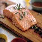 Filet of salmon topped with rosemary leaves on a cedar plank
