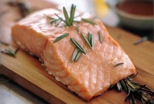 Filet of salmon topped with rosemary leaves on a cedar plank