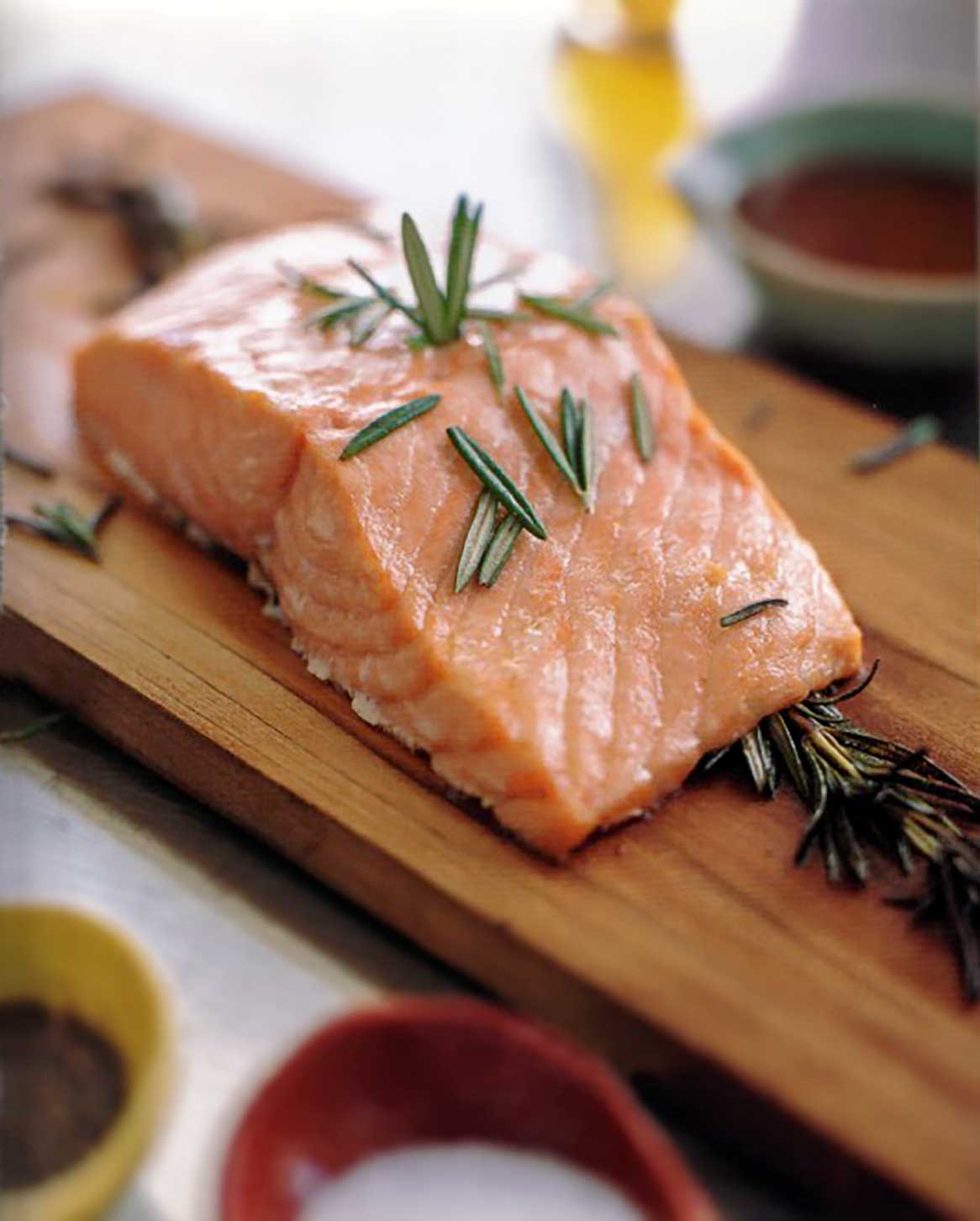 Filet of salmon topped with rosemary leaves on a cedar plank.