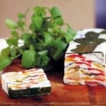 A loaf of tomato-goat cheese terrine--garlicky goat cheese layered with red and yellow tomatoes and arugula on a cutting board