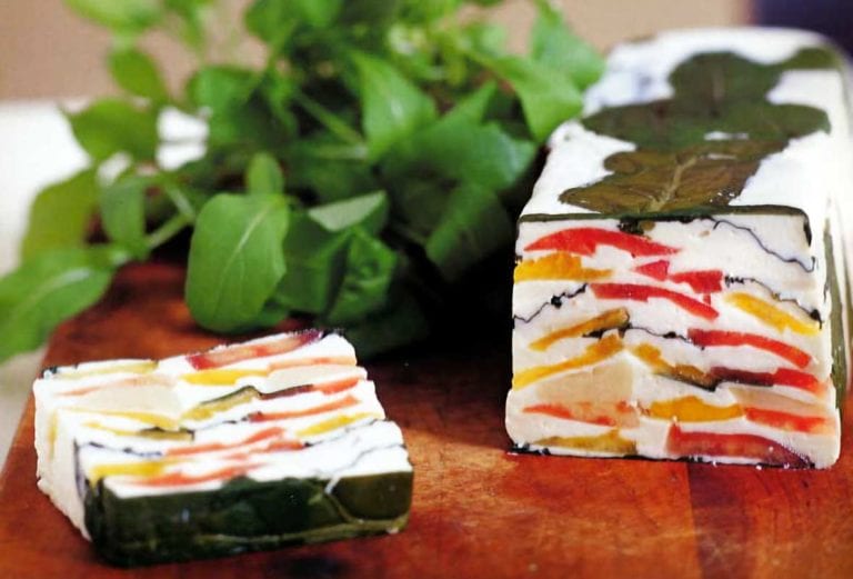 A loaf of tomato-goat cheese terrine--garlicky goat cheese layered with red and yellow tomatoes and arugula on a cutting board