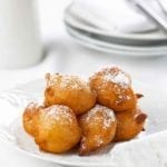 A pile of ricotta-sweet potato beignets dusted with confectioners' sugar on a white plate.