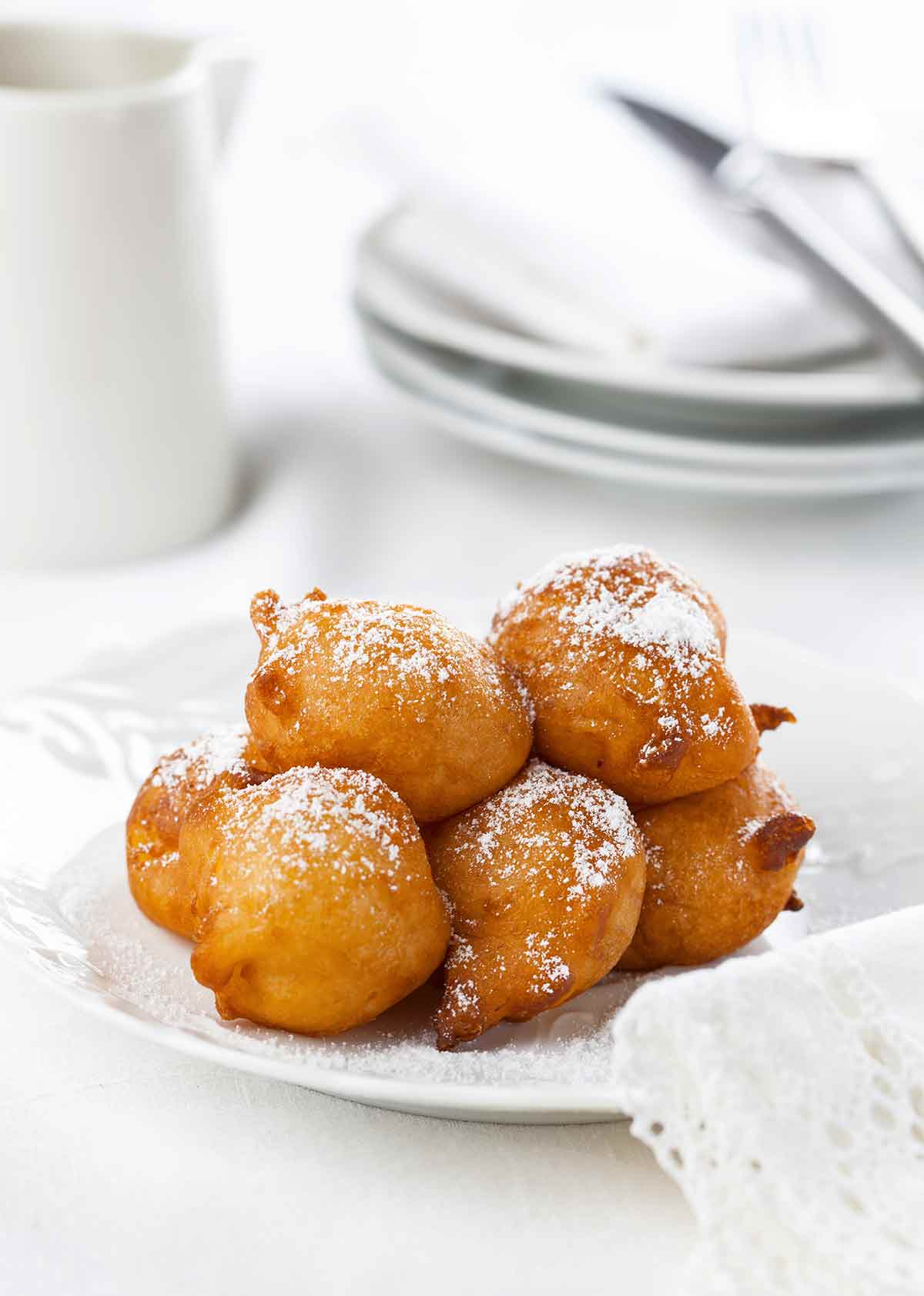 A pile of ricotta-sweet potato beignets dusted with confectioners' sugar on a white plate.