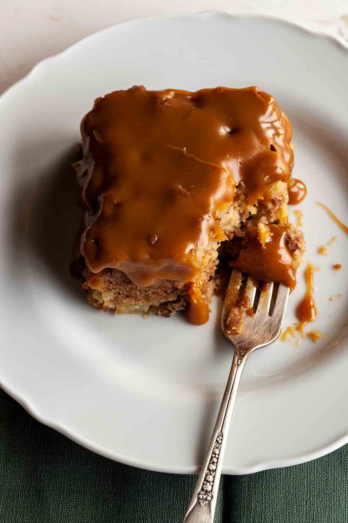 A square of Edna Lewis's apple cake with caramel glaze on a white plate with a fork.