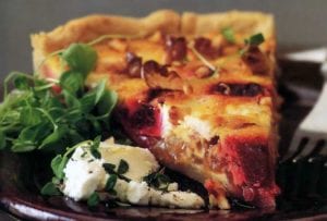 A slice of goat cheese, roasted beet, and walnut tart, goat cheese and watercress on the side