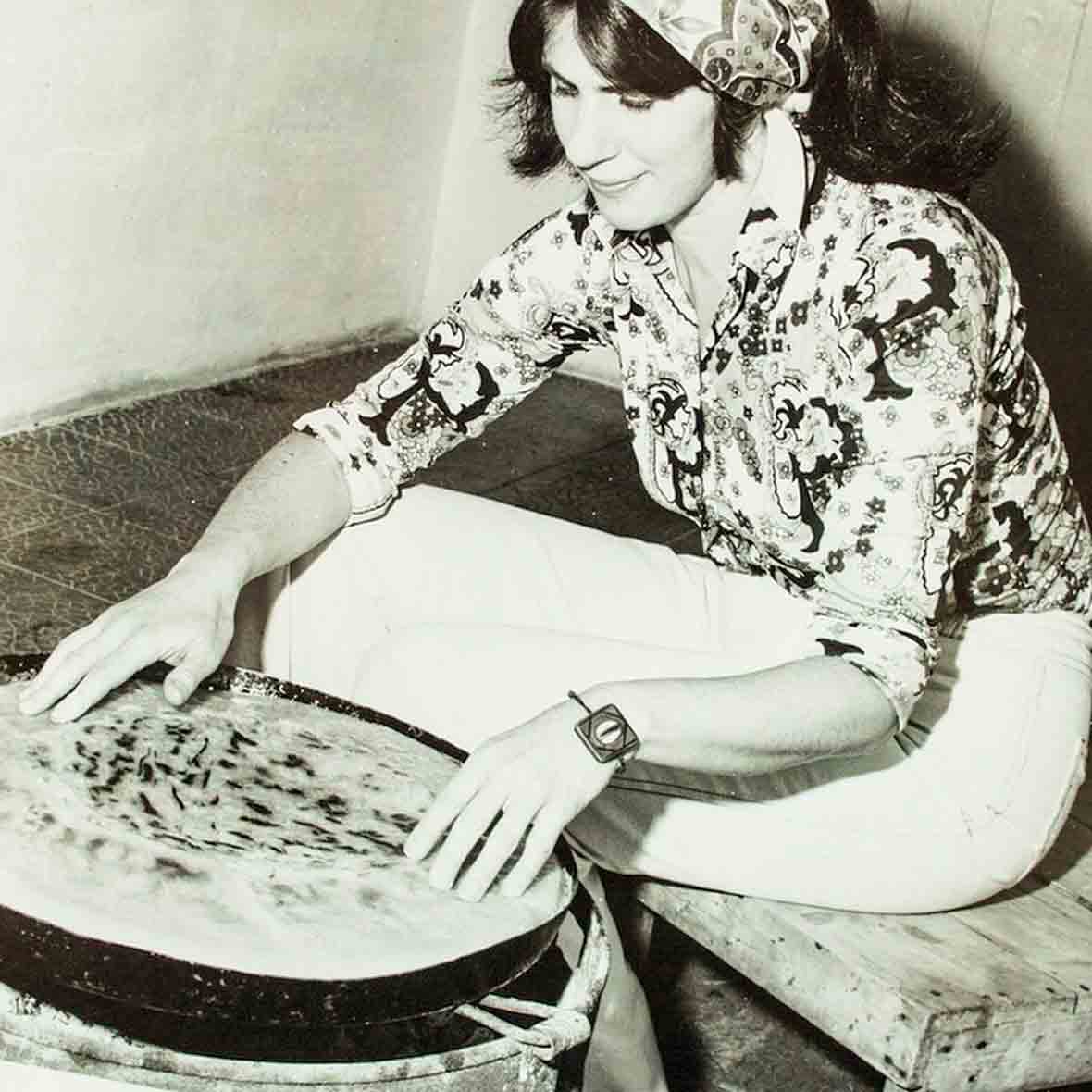 A black and white photo of Paula Wolfert in a head scarf cooking in Morocco.