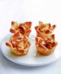 Four mini apple tarts made from apple slices in puff pastry shells on a plate.