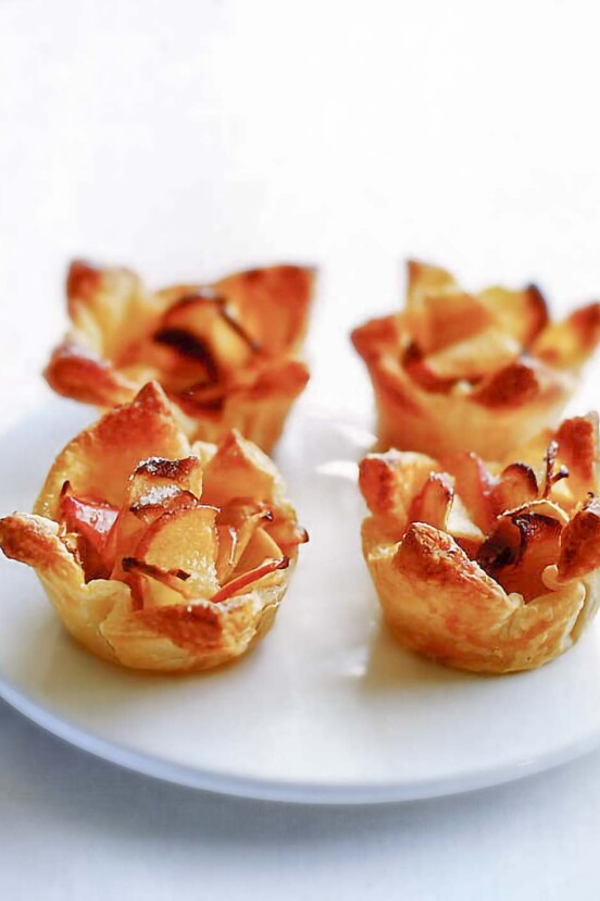 Four mini apple tarts made from apple slices in puff pastry shells on a plate.