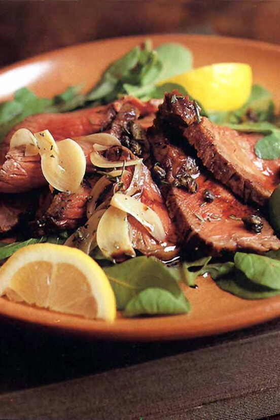 Plate of grilled beef, rosemary, capers, salad greens and lemon wedges.