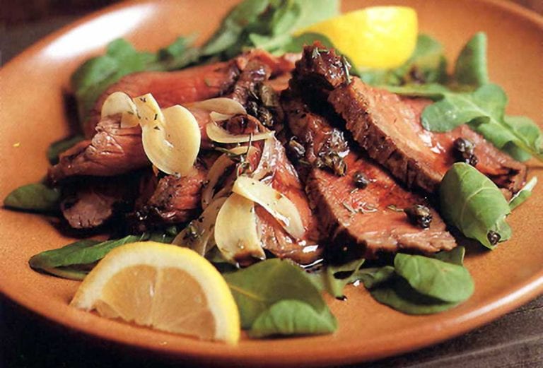 Plate of grilled beef, rosemary, capers, salad greens and lemon wedges