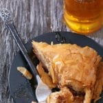 Triangular piece of Greek baklava, with layers of filo or phyllo dough filled with chopped walnuts, drizzled with honey on a black plate