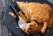 Triangular piece of Greek baklava, with layers of filo or phyllo dough filled with chopped walnuts, drizzled with honey on a black plate