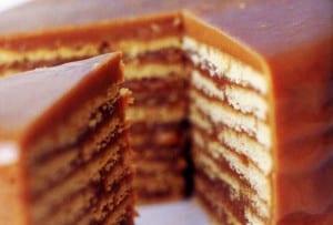 A nine layer butterscotch cake with one slice being removed from it.