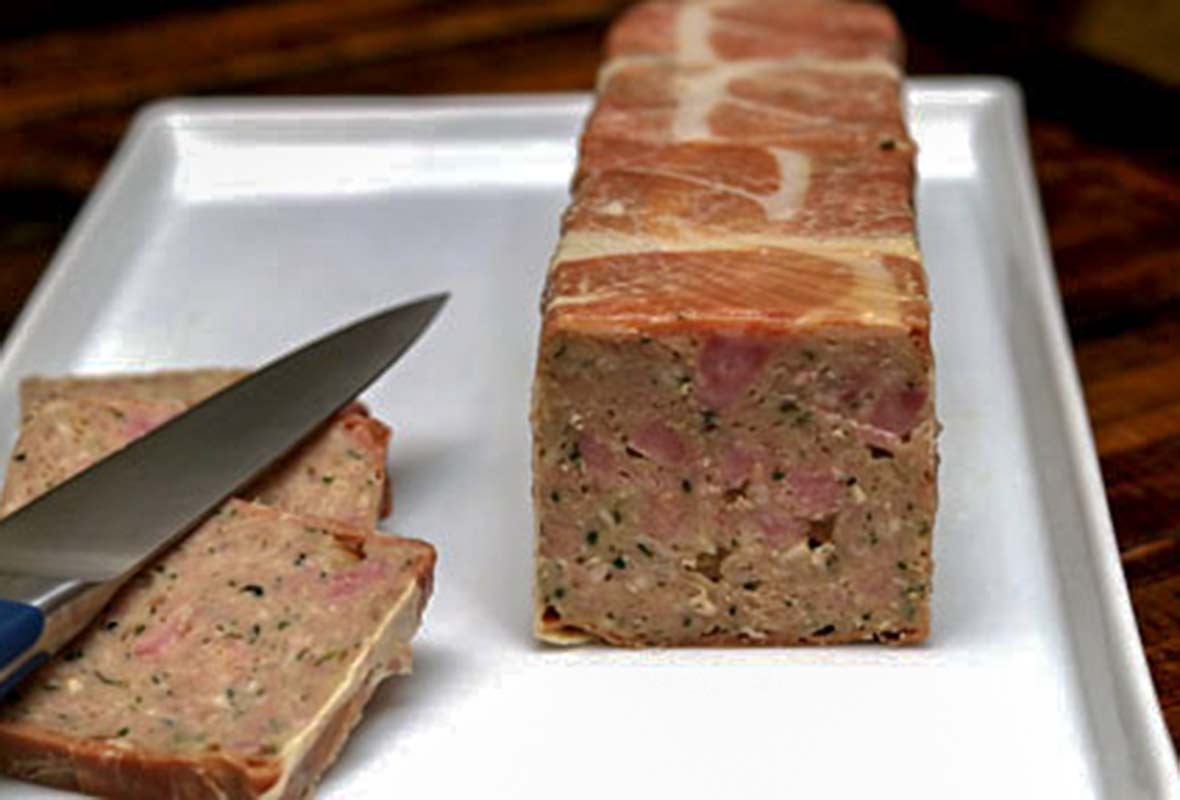 A terrine of country pate with 2 slices cut and a knife resting on top