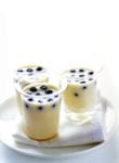 Three glasses of blueberry and white chocolate mousse dotted with blueberries, on a white tray
