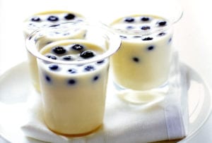 Three glasses of blueberry and white chocolate mousse dotted with blueberries, on a white tray