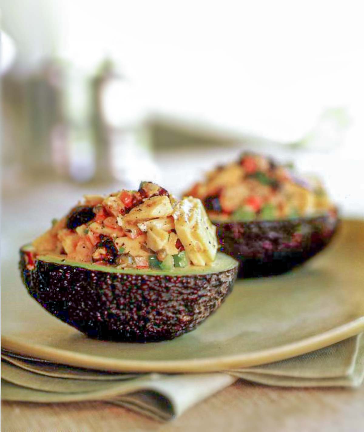 Two avocado halves filled with fresh tuna with dry-cured black olives.